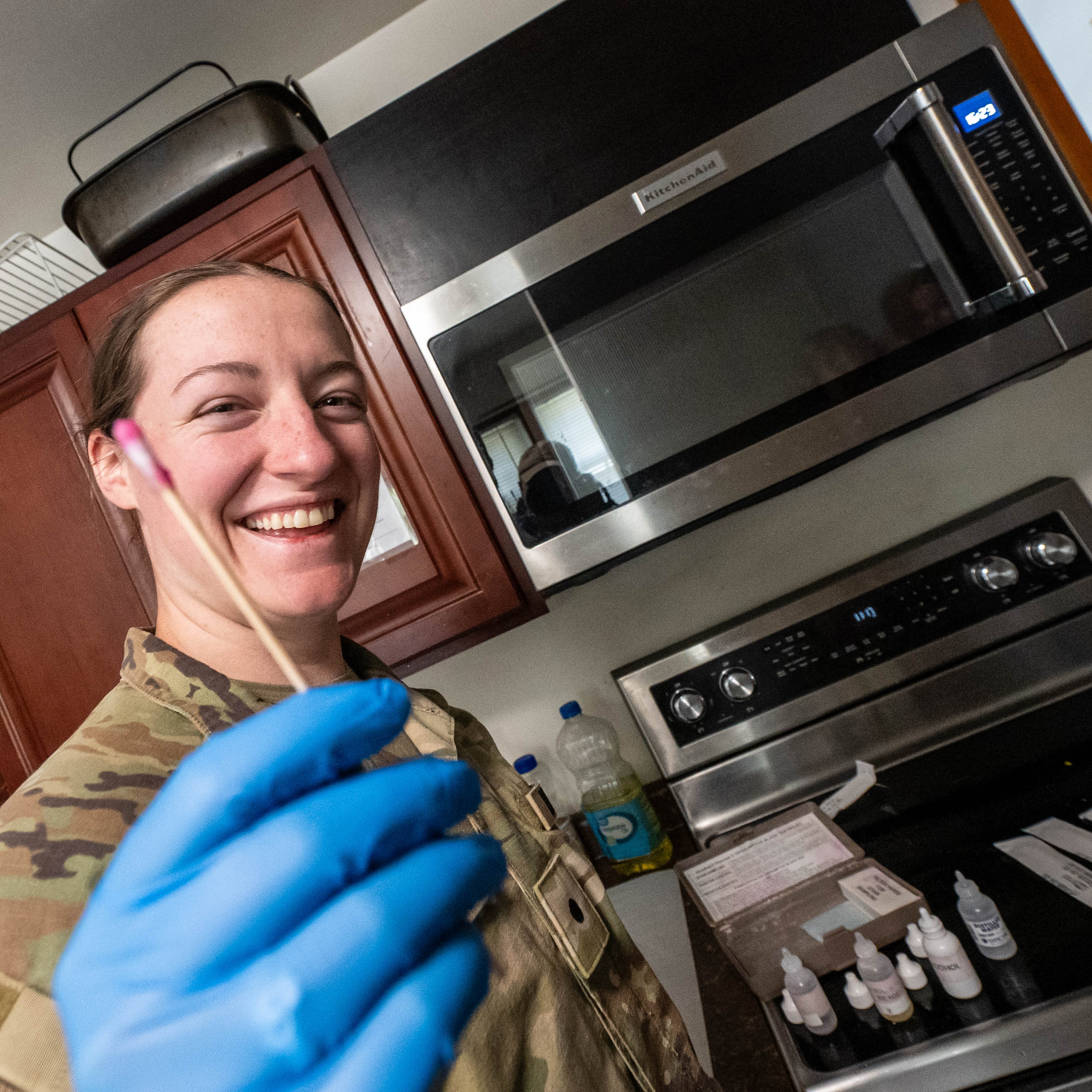 Uniformed person wearing blue gloves holds up a swab in a kitchen.