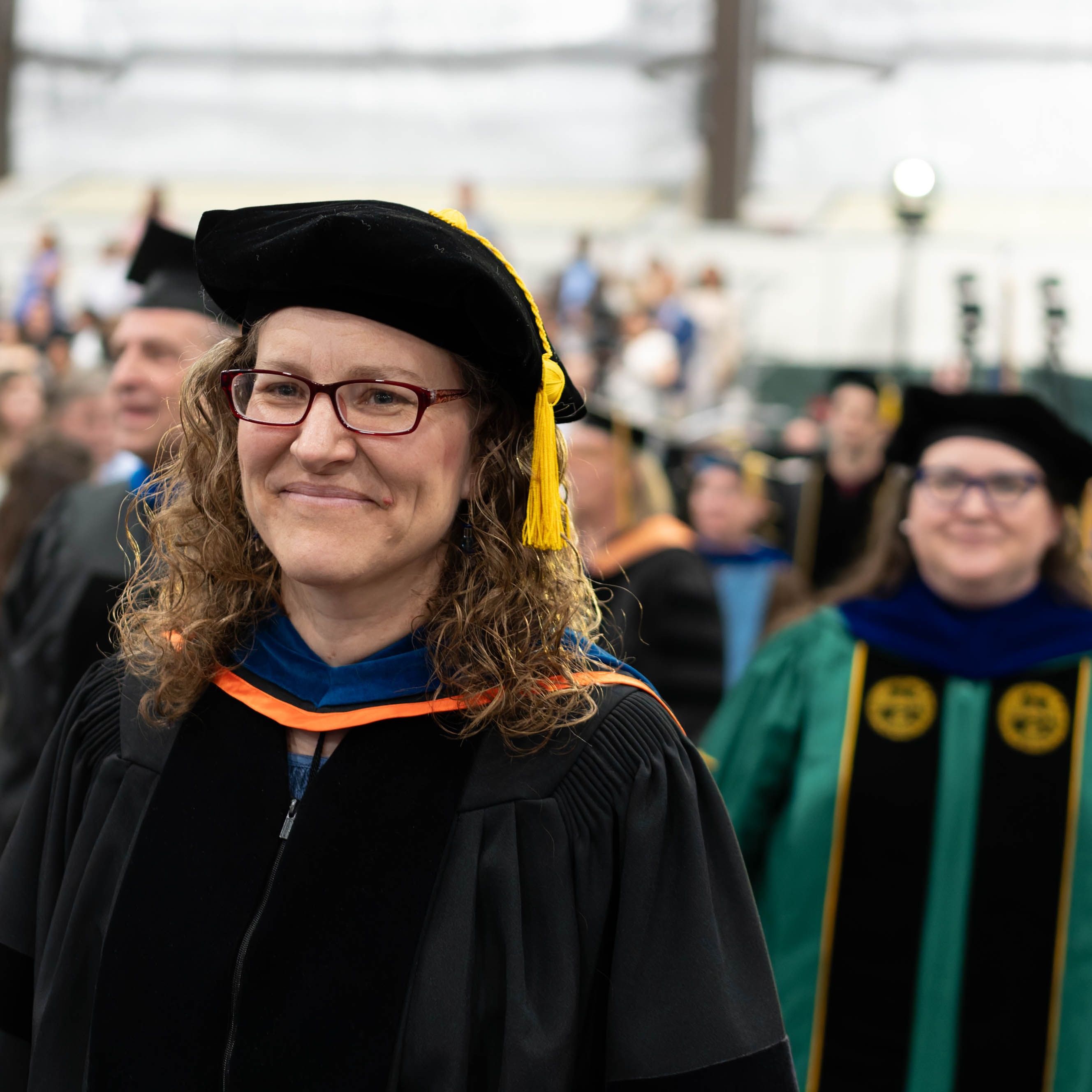 Person in academic regalia and tam walks in a graduation procession.