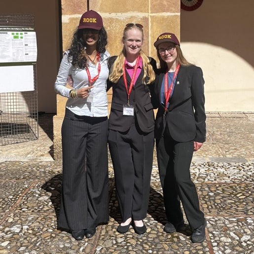 Three students wearing ROOK hats and conference badges stand in front of a stone column outdoors.