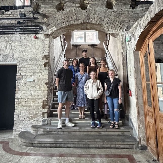 Eight people stand on stone steps beneath a brick archway inside a historic building.