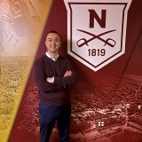 Person standing with arms crossed in front of a Norwich University banner displaying the founding year 1819 and the university emblem.