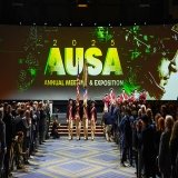 A group in revolutionary clothing holding flags marches down an aisle between crowds.