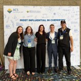 Five people pose with conference badges in front of an ACS Chemistry for Life backdrop.