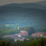 Red brick campus buildings sit among dense green trees with layered forested hills in the background.