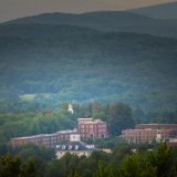 Red brick campus buildings sit among dense green trees with layered forested hills in the background.