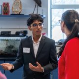 Student in a suit speaks with another person in a classroom.