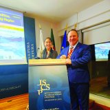 Two people stand at an ISCTE podium in a conference room with flags and presentation screens behind them.
