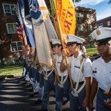 Norwich cadets stand in formation carrying flags and a rifle.