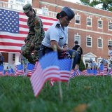 Cadets place small U.S. flags in the grass in front of a large U.S. flag and campus building.