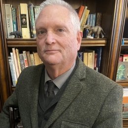 A photo of Dr. Marvin Lutnesky in a suit and tie in front of a bookcase with books and a small elephant statue.