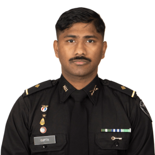 Person in a black uniform with badges, name tag reading “Gupta,” shoulder epaulets, and decorative pins.