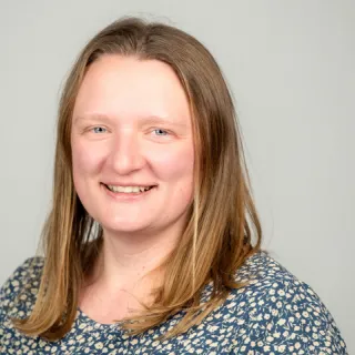 Person with medium colored straight shoulder length hair, light complexion, wearing a green patterned shirt.