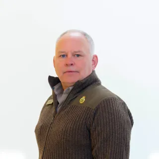 Person in a dark suit, blue shirt, and patterned tie poses against a plain light background.