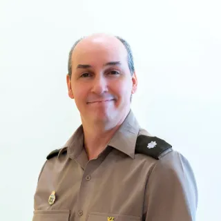Person in a gray uniform shirt with insignia poses against a plain light background.