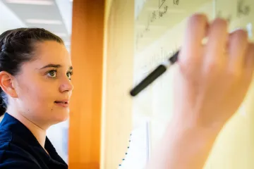 Norwich Mathematics Student Writing Complex Formulas on Whiteboard