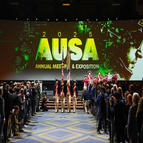 A group in revolutionary clothing holding flags marches down an aisle between crowds.