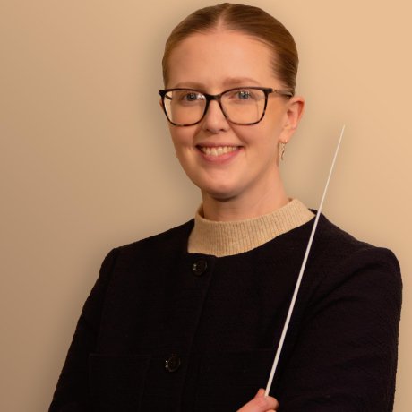 Person in a dark jacket holds a thin baton against a plain background.