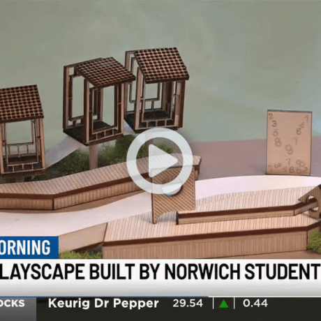 Model of a wooden playscape with small structures and ramps shown in a news graphic labeled “Library Playscape Built by Norwich Students.”