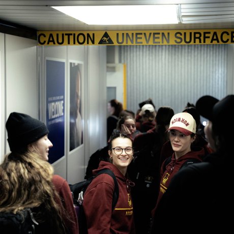 Students in Norwich hockey hoodies walk through a jet bridge beneath a caution uneven surface sign.