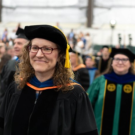 Person in academic regalia and tam walks in a graduation procession.