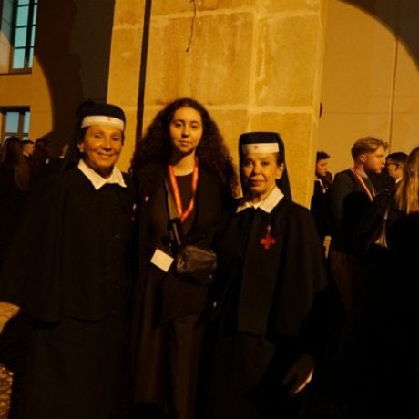 Student poses with two nuns outside a stone building at night.