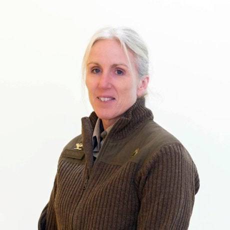 Person with light hair wears a brown zip-up sweater and collared shirt against a plain white background.