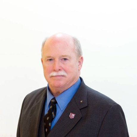 Person in a dark suit, blue shirt, and patterned tie poses against a plain light background.