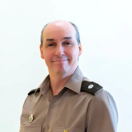 Person in a gray uniform shirt with insignia poses against a plain light background.