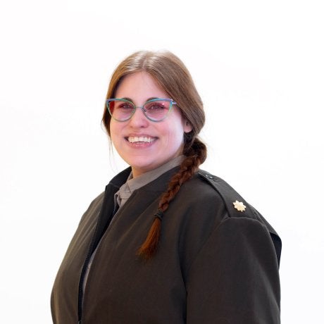 Person with glasses and a braid wears a dark coat and faces the camera.