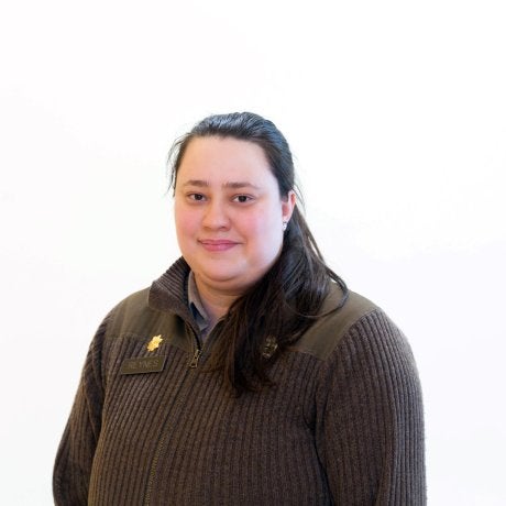 Person with long hair wears a dark sweater and faces the camera against a white background.
