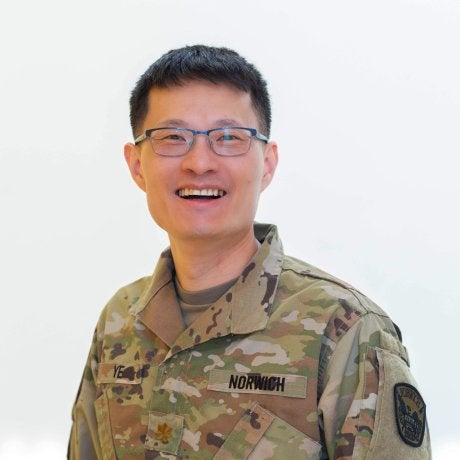 Person wearing glasses and a Norwich camouflage uniform faces the camera against a light background.
