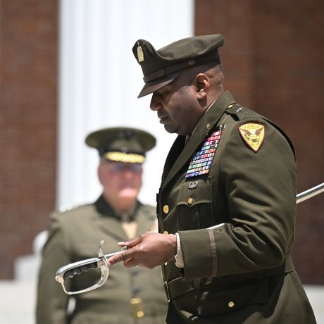 Uniformed officer holds a ceremonial sword during an outdoor military ceremony.