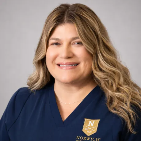 Person with curly hair wears navy Norwich University School of Nursing scrubs.