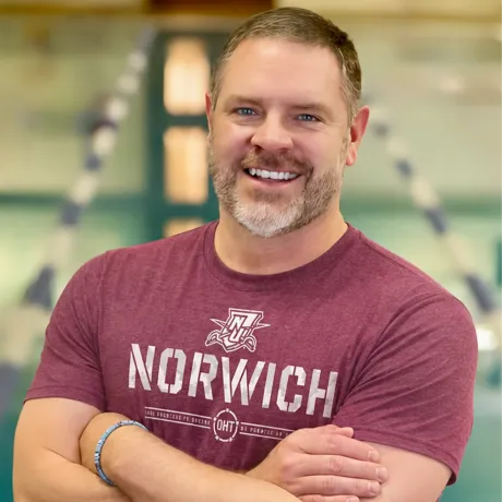 Portrait of a person wearing a Norwich T-shirt with arms crossed.