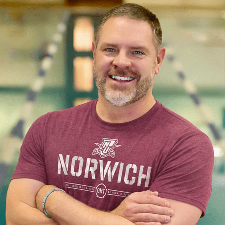 Portrait of a person wearing a Norwich T-shirt with arms crossed.