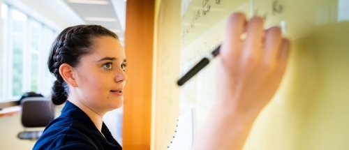 Norwich Mathematics Student Writing Complex Formulas on Whiteboard