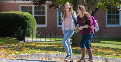 Two Norwich students in civilian clothing walking across campus on a sunny fall day.
