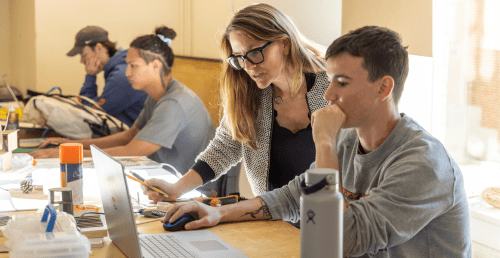 Student working on computer with faculty member assisting.