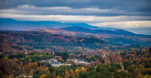 Aerial photo of Norwich's campus in the fall, with colorful foliage and blue mountains in the distance.