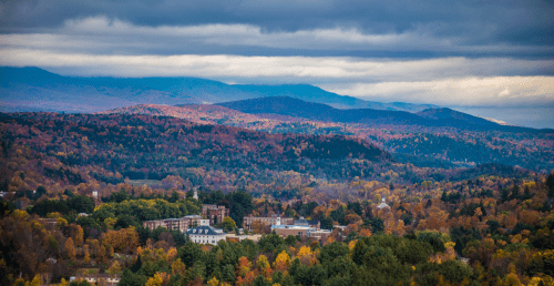 Aerial photo of Norwich's campus in the fall, with colorful foliage and blue mountains in the distance.