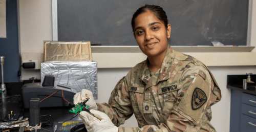 Student in science lab and wearing military uniform while she works on a technical project.