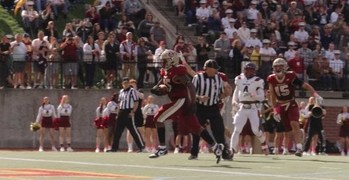 Norwich football player runs with the ball as teammates and defenders follow.