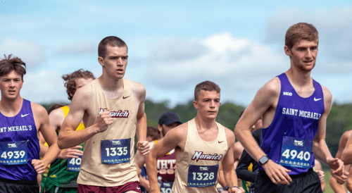 College cross-country runners from Norwich competing in a race under partly cloudy skies.