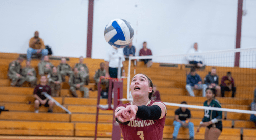Norwich volleyball player prepares to bump the ball during a match, with focused spectators watching from the bleachers.
