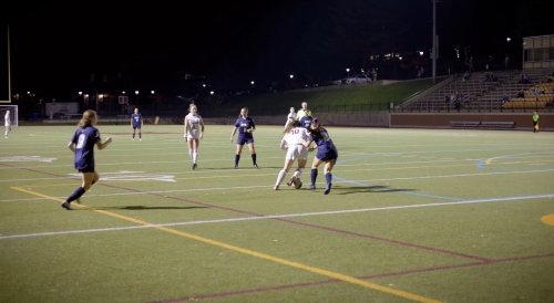 Women's soccer players competing for the ball on a field at night.