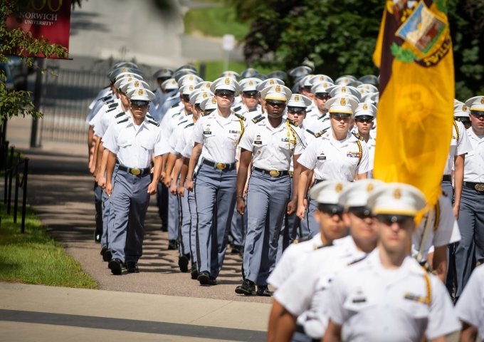 Norwich University Corps of Cadets in dress blues, marching across campus.