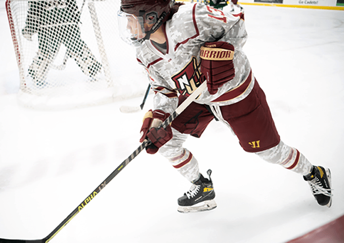 A hockey player in a military-themed camouflage uniform competing against opponent in green and yellow stripes, with teammates visible in the background.