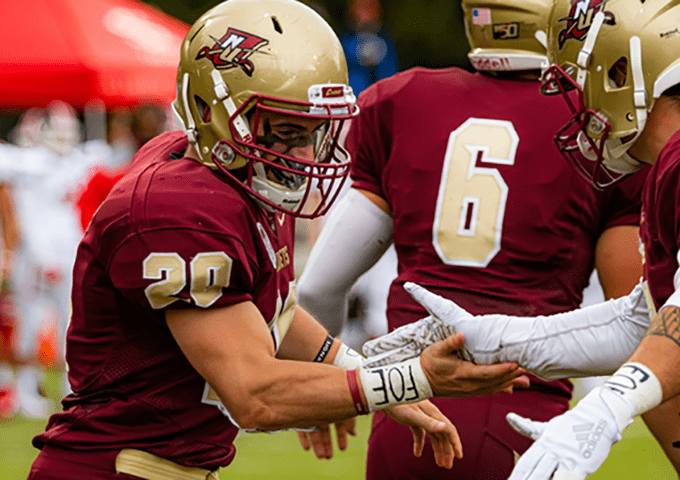 College football players in maroon and gold uniforms celebrating together, with player number 20 in foreground and number 6 visible on teammate's jersey.
