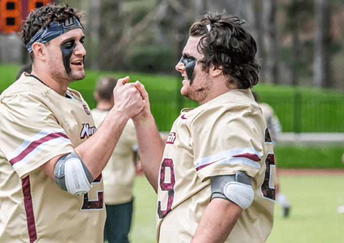 Two players, faces marked with eye black, share a handshake or celebratory gesture, showing camaraderie and intensity on the field.