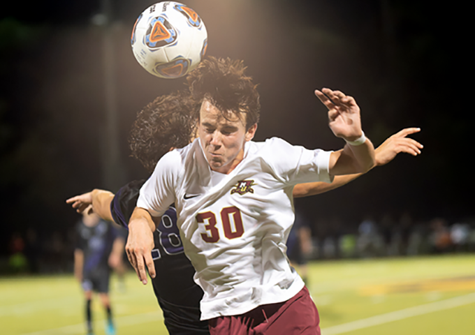 Two soccer players compete for a header during a night game, with player number 30 in white jersey positioning himself beneath the ball.